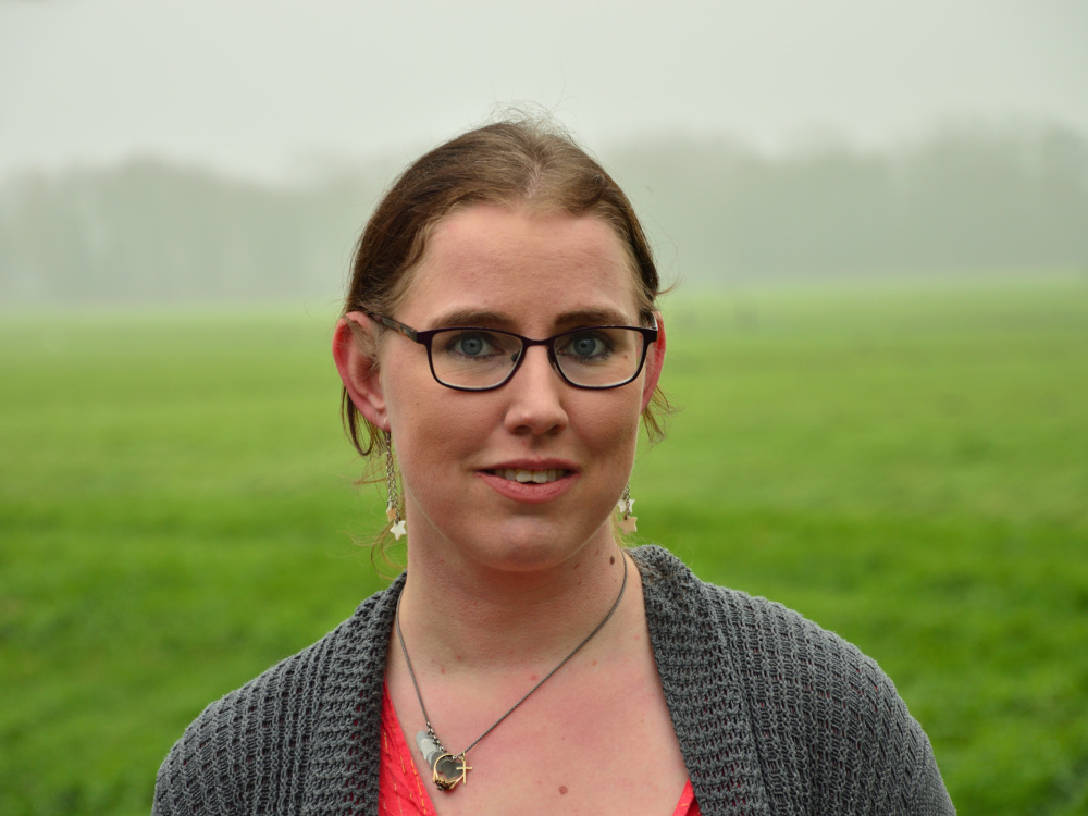 Foto van Lonneke Tomas, een witte vrouw met een bril en donkerblond, opgestoken haar. Ze draagt een rood t-shirt en grijs vest.